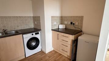 A compact kitchen with a washing machine, a small refrigerator, and a countertop with a sink.