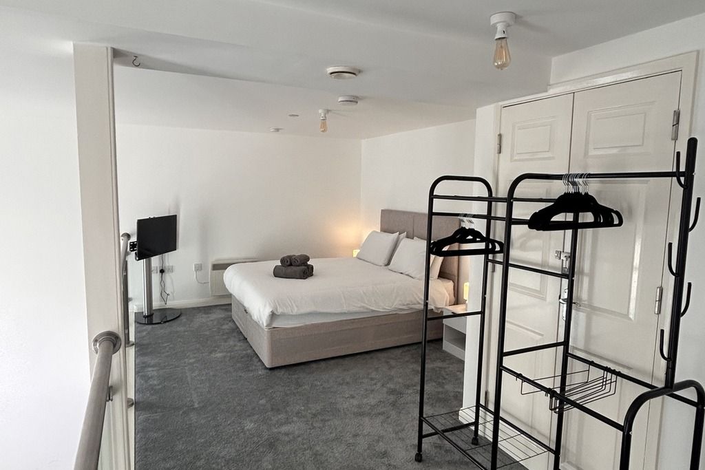 Une chambre à coucher comprenant un lit, une armoire, une table de chevet, une lampe et un porte-vêtements.