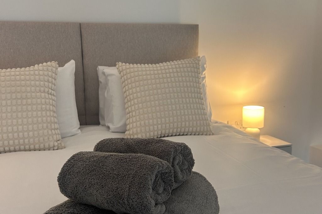 A neatly made bed with pillows and a folded towel, a bedside lamp, and a headboard.
