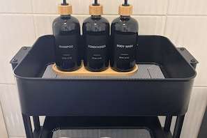 En svart metallhylla med tre flaskor märkta med ”schampo”, ”balsam” och ”duschkräm”.