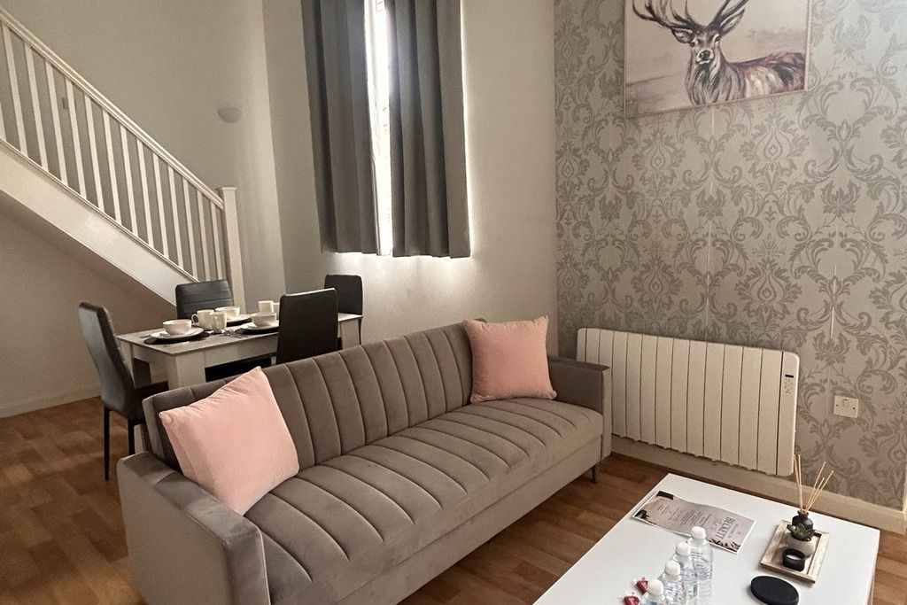 En stue med sofa, sofabord, spisebord med stole, en radiator og en trappe.