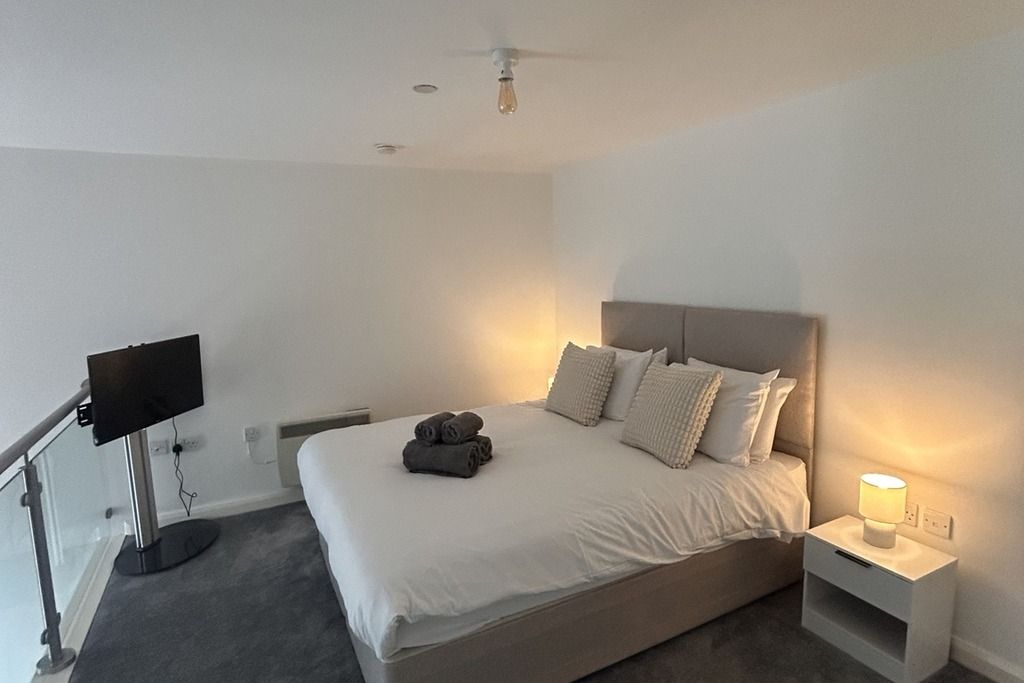 Una habitación de hotel con cama, lámpara de noche, televisor de pantalla plana y ventilador de techo.