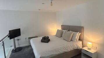 Una habitación de hotel con cama, lámpara de noche, televisor de pantalla plana y ventilador de techo.