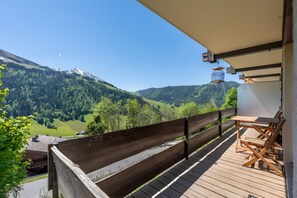A wooden deck with a table and chairs, overlooking a mountainous landscape with green fields and a clear sky. - Apartment 'Soladret' with Mountain View and Balcony (La Clusaz)