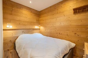 Ein Zimmer mit Holzwänden, einem Bett, zwei Wandleuchten und einem kleinen Regal.