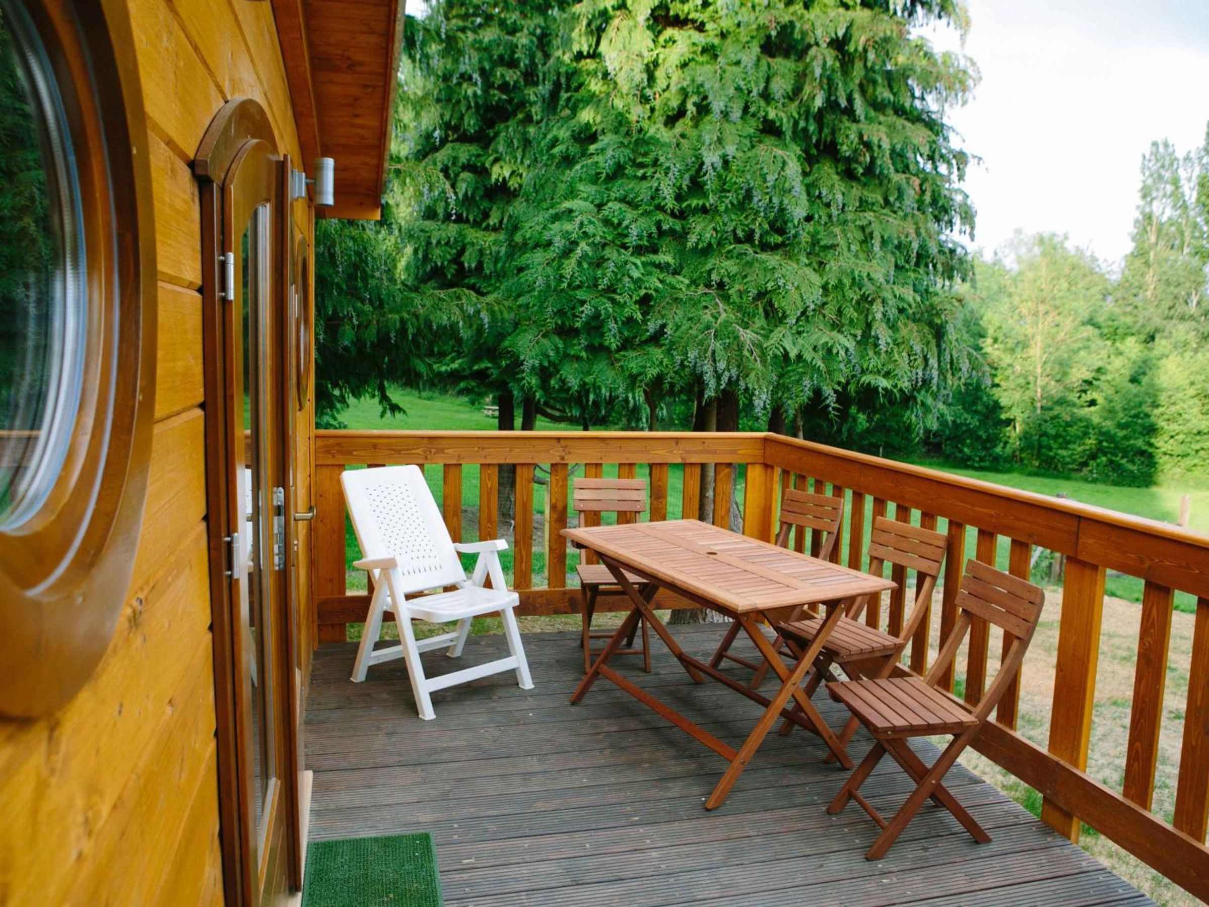 Une terrasse en bois avec une table et des chaises, donnant sur une zone boisée.