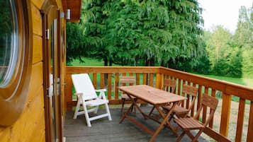 Une terrasse en bois avec une table et des chaises, donnant sur une zone boisée.