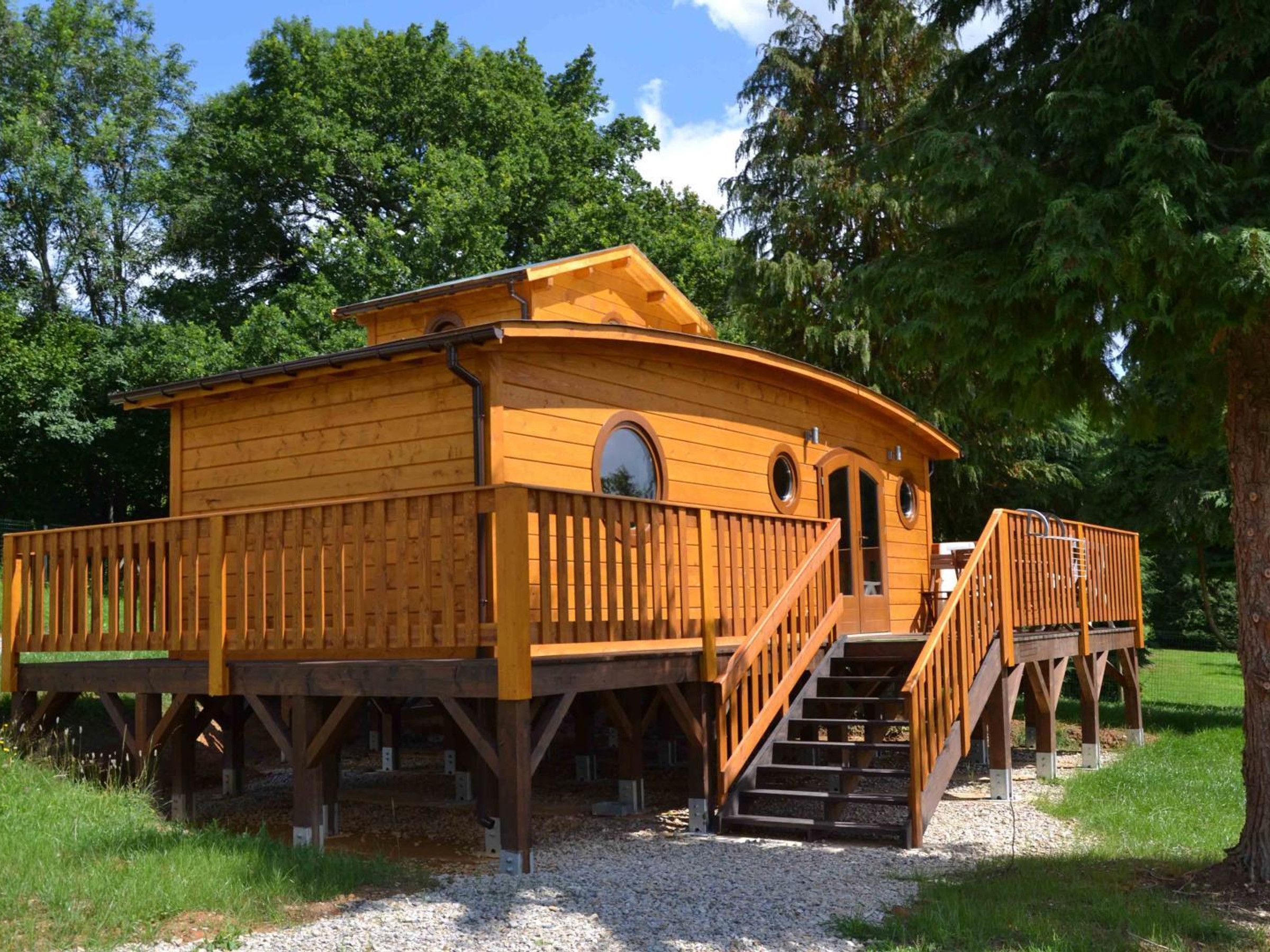 Eine Holzhütte mit einer Terrasse und Treppe, umgeben von Bäumen.