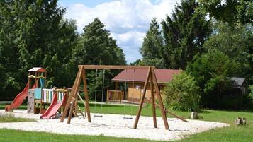 A playground with swings and slides, surrounded by trees and a building with a red roof.