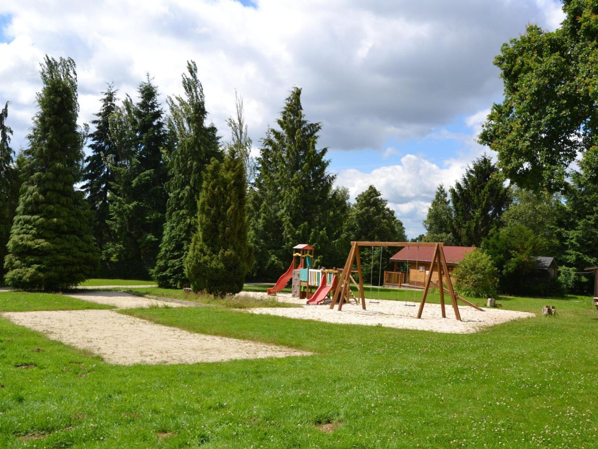 A playground with a swing set and a slide, surrounded by trees and a grassy area.