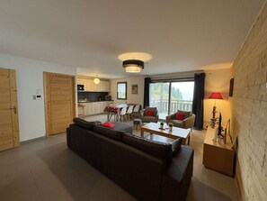 A modern living room with a sofa, a dining table, and a kitchen in the background. - Apartment with south-facing balcony, mountain view - 6 guests (Auris)