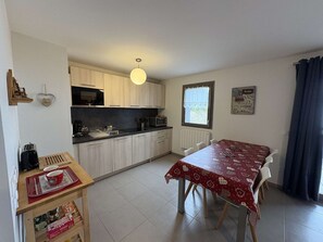 A compact kitchen with a dining table, a hanging light fixture, and a window with a view. - Apartment with south-facing balcony, mountain view - 6 guests (Auris)