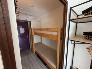 Ein Stockbett mit einer Leiter, einer Holztür und einem Regal mit einem schwarzen Gegenstand obenauf.