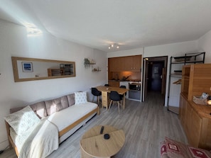 A compact living space with a sofa, a dining table, a kitchen area, and a small round table with a remote control. - Cozy studio with view - 4 guests (Flaine)