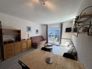 Ein gemütliches Wohnzimmer mit einem Holzesstisch, einer Couch und einem Balkon mit Blick auf ein bewaldetes Gebiet.