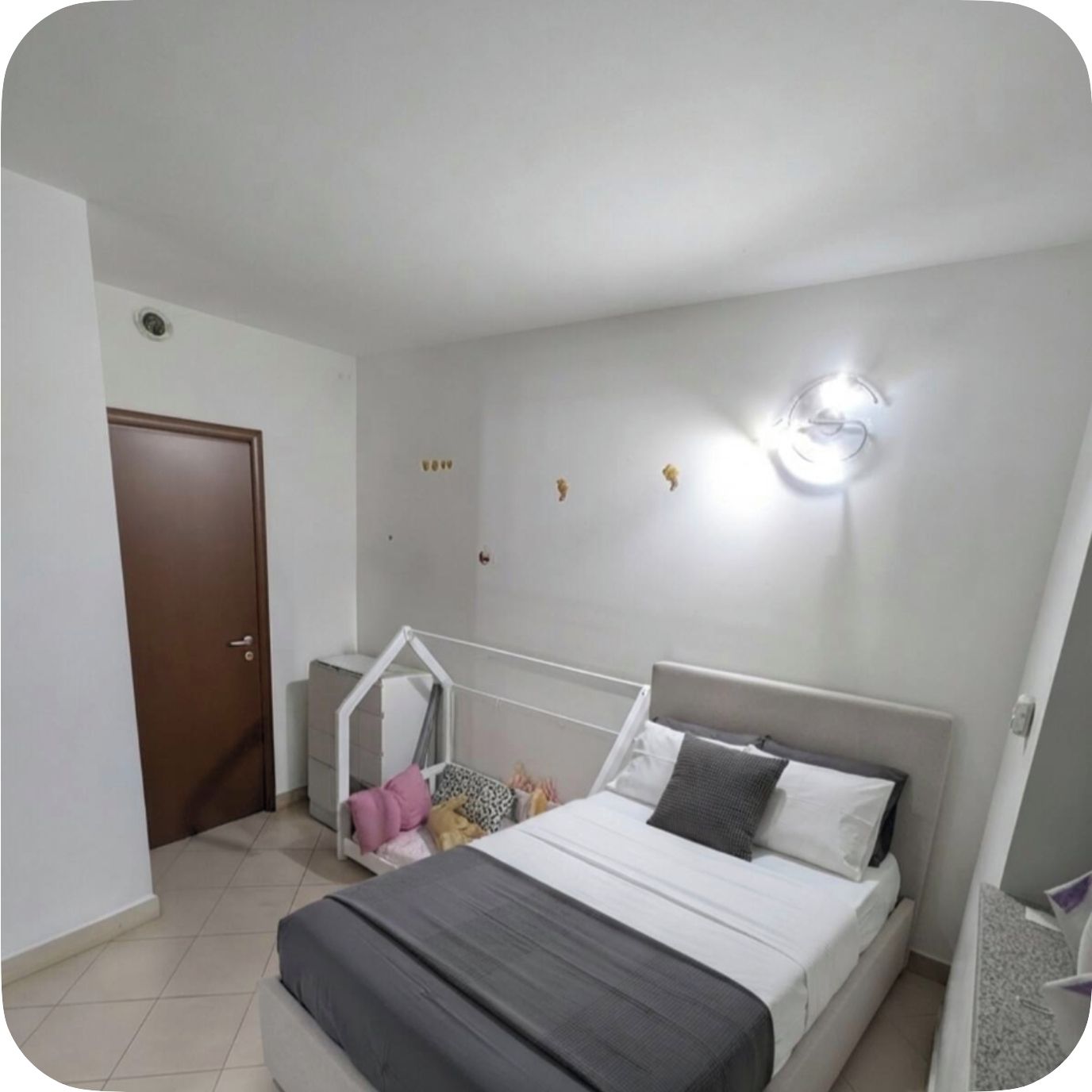 Una camera da letto con un letto, un armadio, un piccolo angolo salotto e un punto luce a parete.