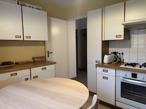 Eine kleine Küche mit weißen Schränken, einem runden Holztisch und einem eingebauten Backofen.