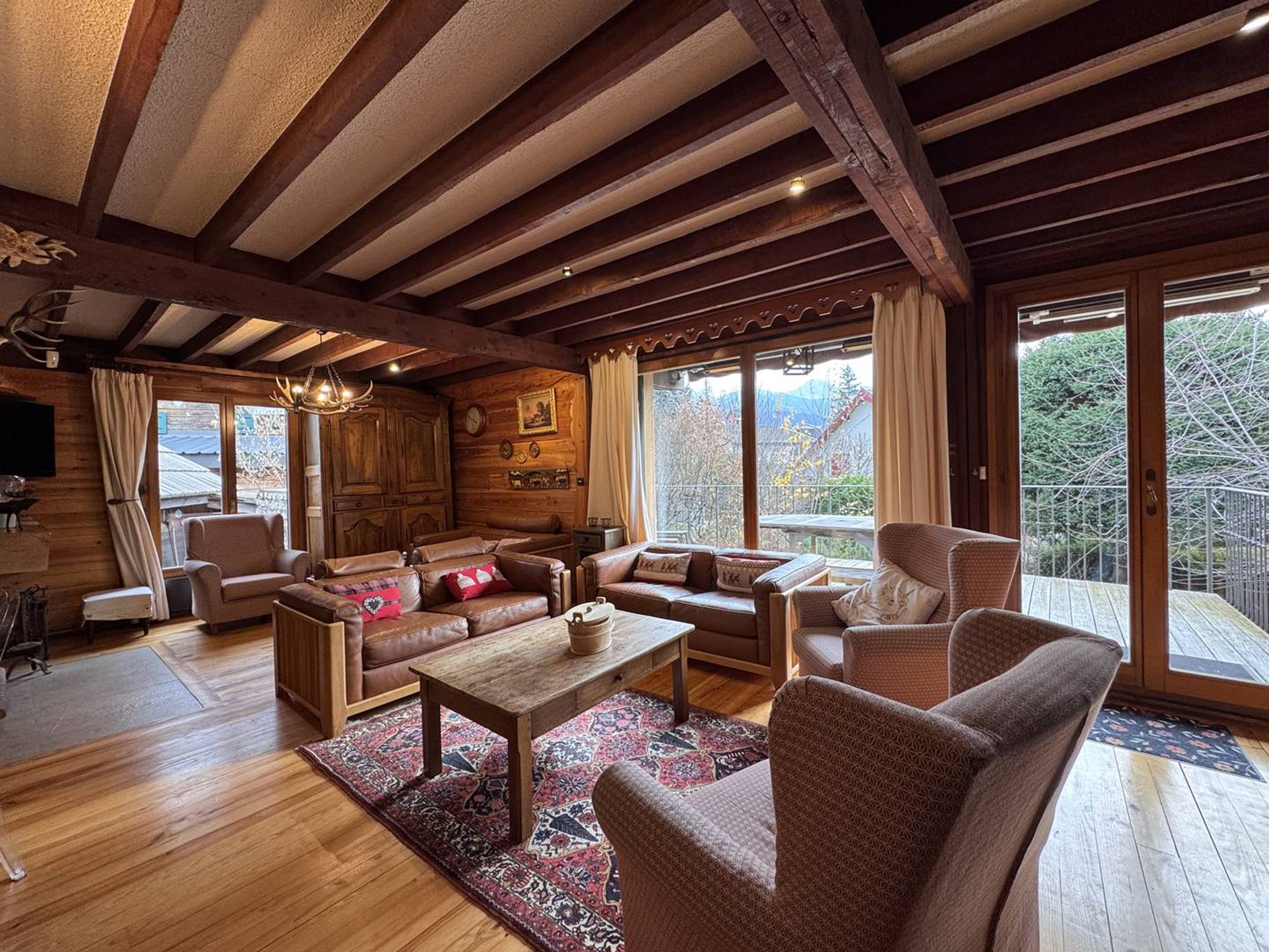 A cozy log cabin interior with wooden beams, leather furniture, and large windows offering scenic views.
