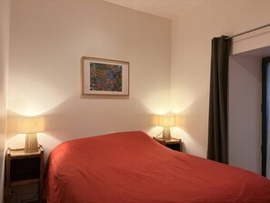 A hotel room with a bed, two bedside lamps, a framed artwork on the wall, and a curtain on the window. - Cozy apartment in Villard-de-Lans - 6 guests (Villard-de-Lans)
