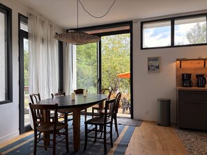 A dining area with a round table, chairs, a hanging light fixture, and a view through a glass door to an outdoor area with trees. - Cozy apartment in Villard-de-Lans - 6 guests (Villard-de-Lans)