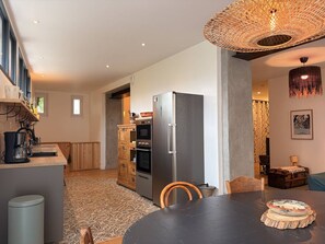 Eine moderne Küche mit Kühlschrank, Backofen und Kaffeemaschine. Es gibt einen Esstisch mit Stühlen und einem gemusterten Teppich.