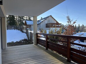 Um deck de madeira com vista para uma paisagem coberta de neve e um edifício com telhado inclinado.
