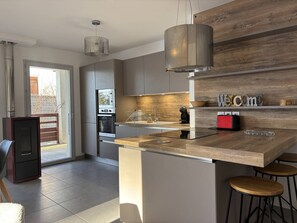 A modern kitchen with a central island, stainless steel appliances, and a wooden accent wall. - Spacious apartment in the heart of Vercors - 6 guests (Villard-de-Lans)