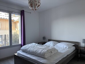 Quarto com cama, mesa de cabeceira, abajur e vista para um edifício lá fora.