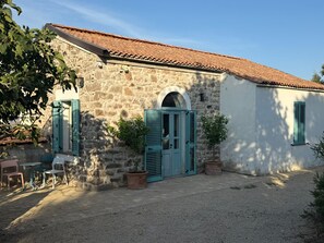 A stone building with a tiled roof, a central arched doorway, and a gravel driveway. - Villa Cabu Abbas (Perfugas)
