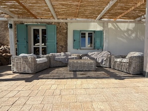 A covered outdoor seating area with wicker furniture and a stone wall. - Villa Cabu Abbas (Perfugas)