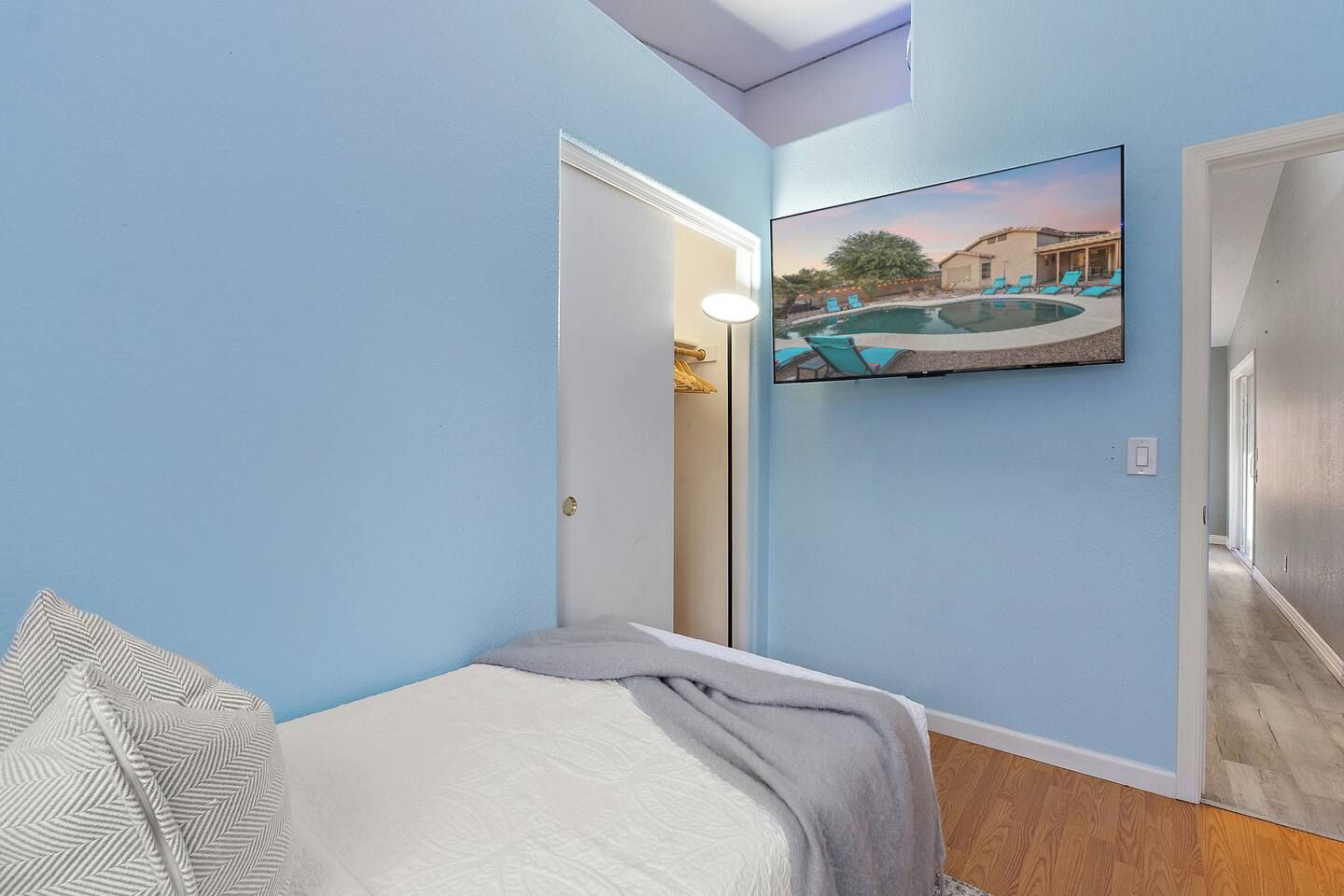 A bedroom with a bed, a painting of a pool, and a hallway leading to another room.