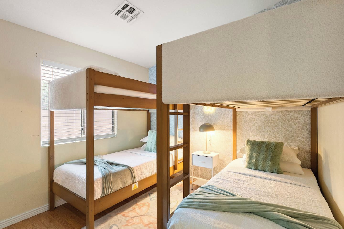Habitación con literas, una mesita de noche con lámpara y pared con diseño.