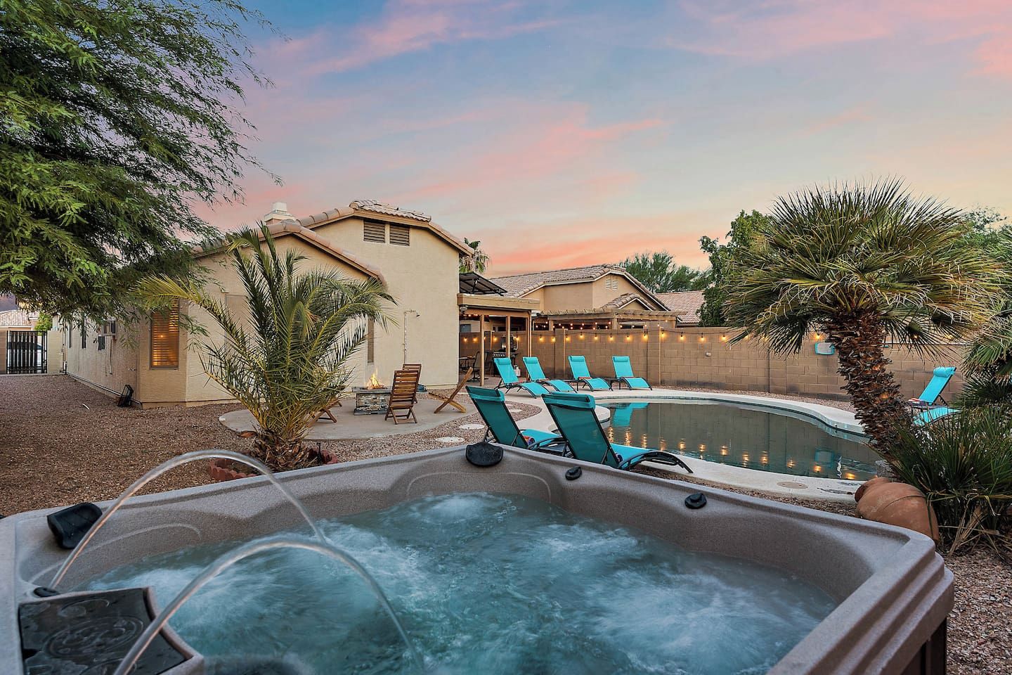 A hot tub with lounge chairs, a swimming pool, and a house with outdoor seating.