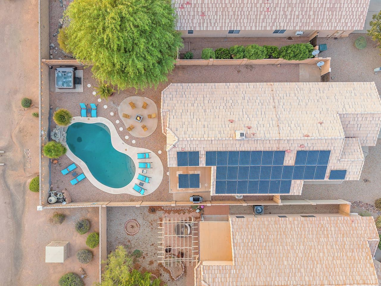 An aerial view of a property with a swimming pool, lounge chairs, a hot tub, and solar panels.