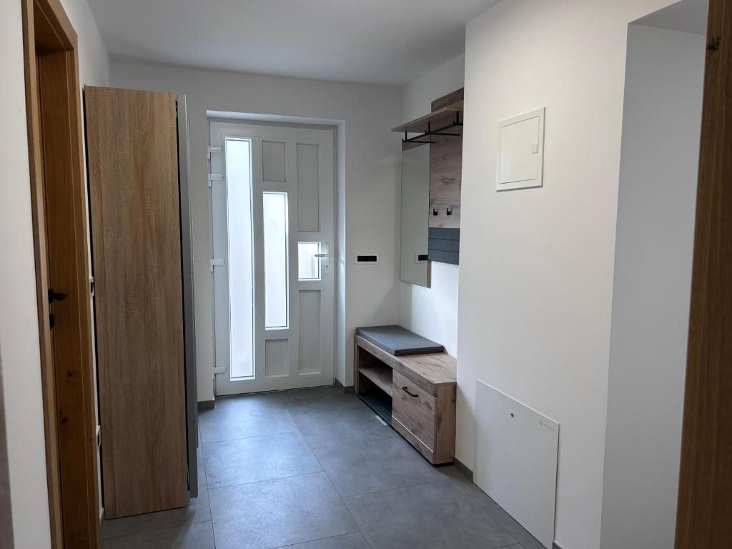 Un pasillo con una puerta de madera, un banco y un estante fijado a la pared.