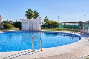 Une piscine à l’eau d’un bleu cristallin, entour ée d’une terrasse dallée et d’un petit bâtiment doté d’un toit rouge.