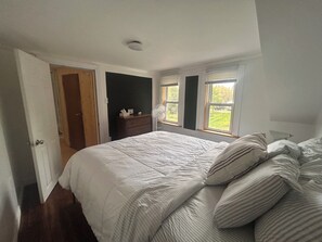 A bedroom with a large bed, a dresser, and a window with a view.
