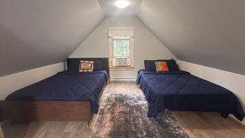 A small, triangular attic bedroom with two beds, a window with a view, and a ceiling light.