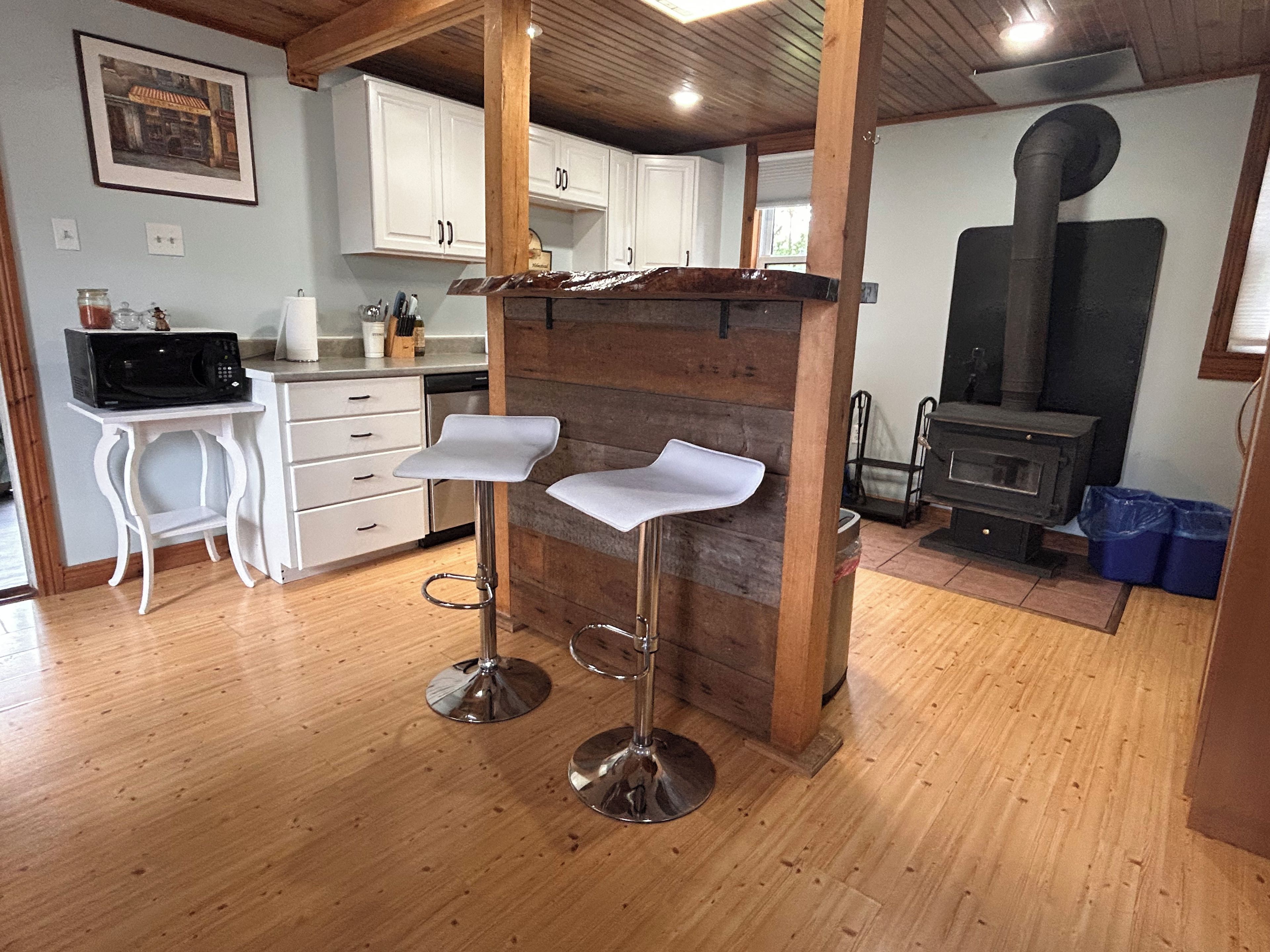 A kitchen with white cabinets, a wooden bar stool, and a wood-burning stove.