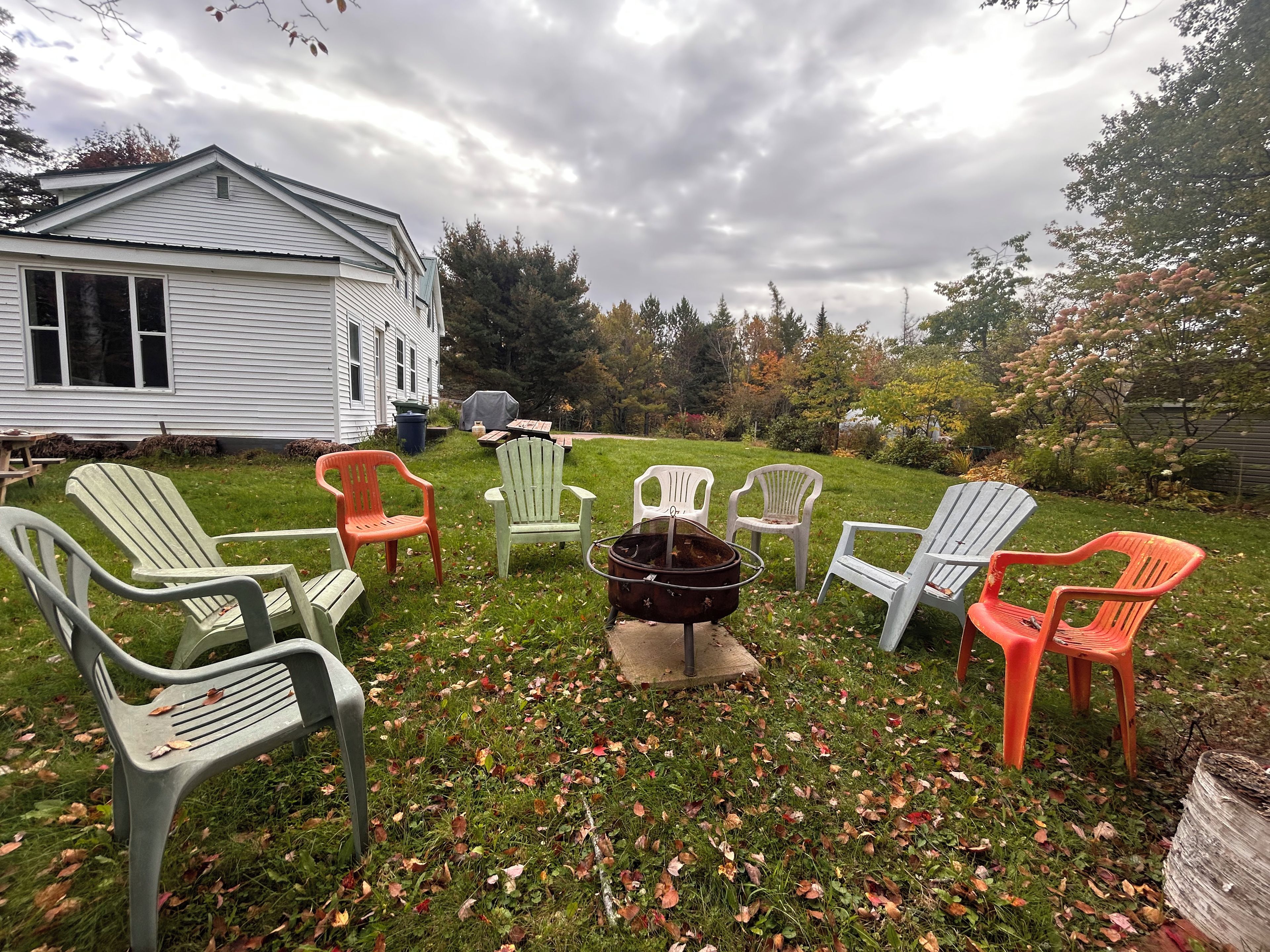A backyard with several Adirondack chairs, a grill, and a small shed.