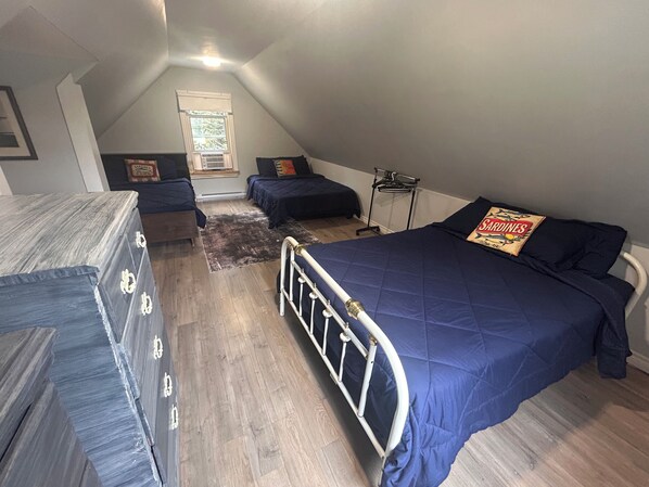 A small, triangular attic bedroom with two beds, a wardrobe, and a window.
