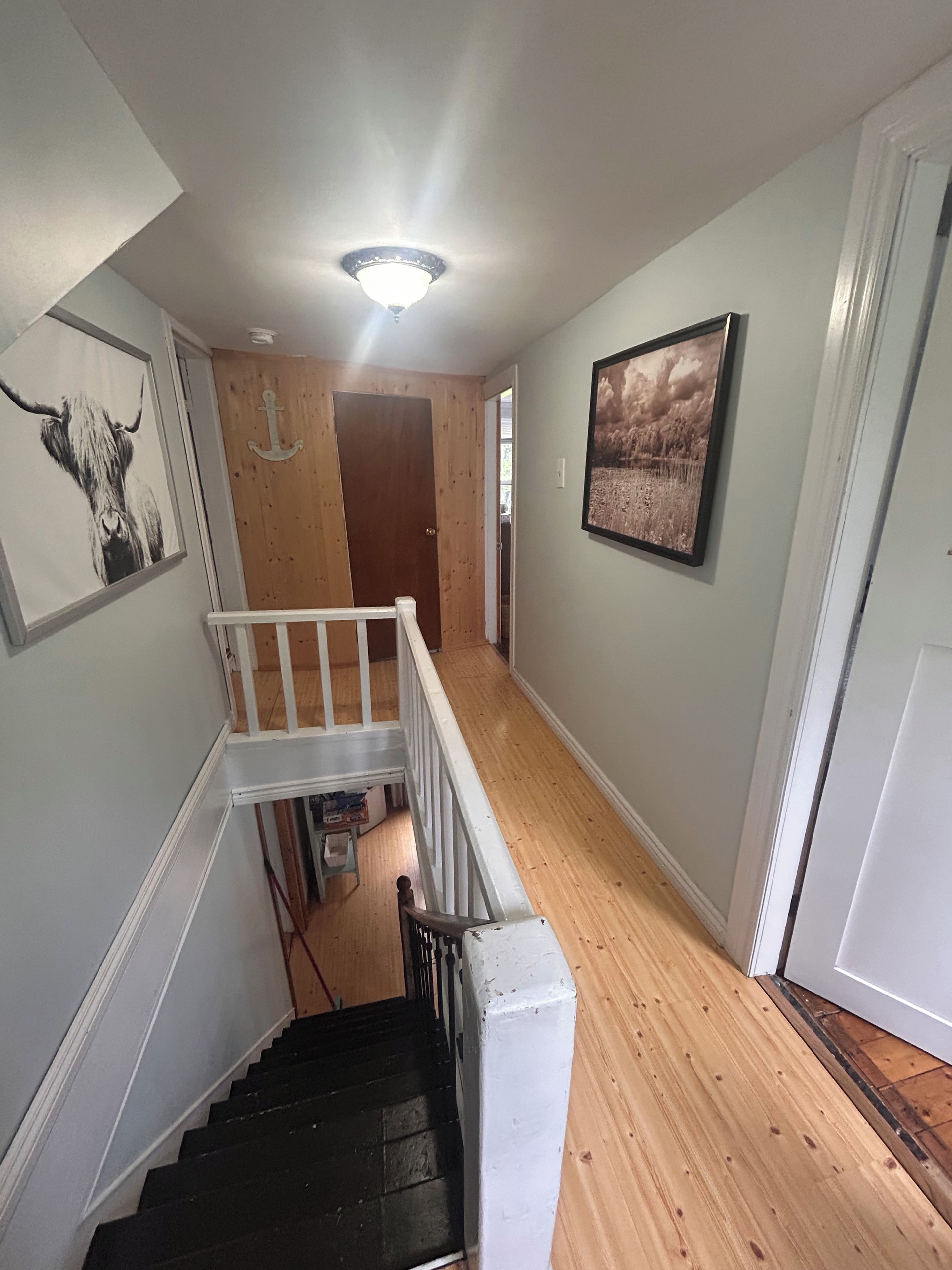 A staircase with a white railing leading to a wooden floor, a ceiling light, and a door with an anchor decoration.