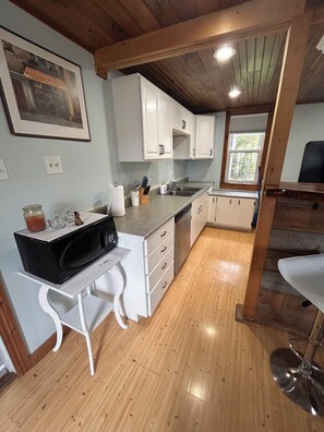 A kitchen with white cabinets, a wooden countertop, a built-in microwave, and a window with a view of trees. - The Happy Helmstead Farmhouse (Tidnish Bridge)