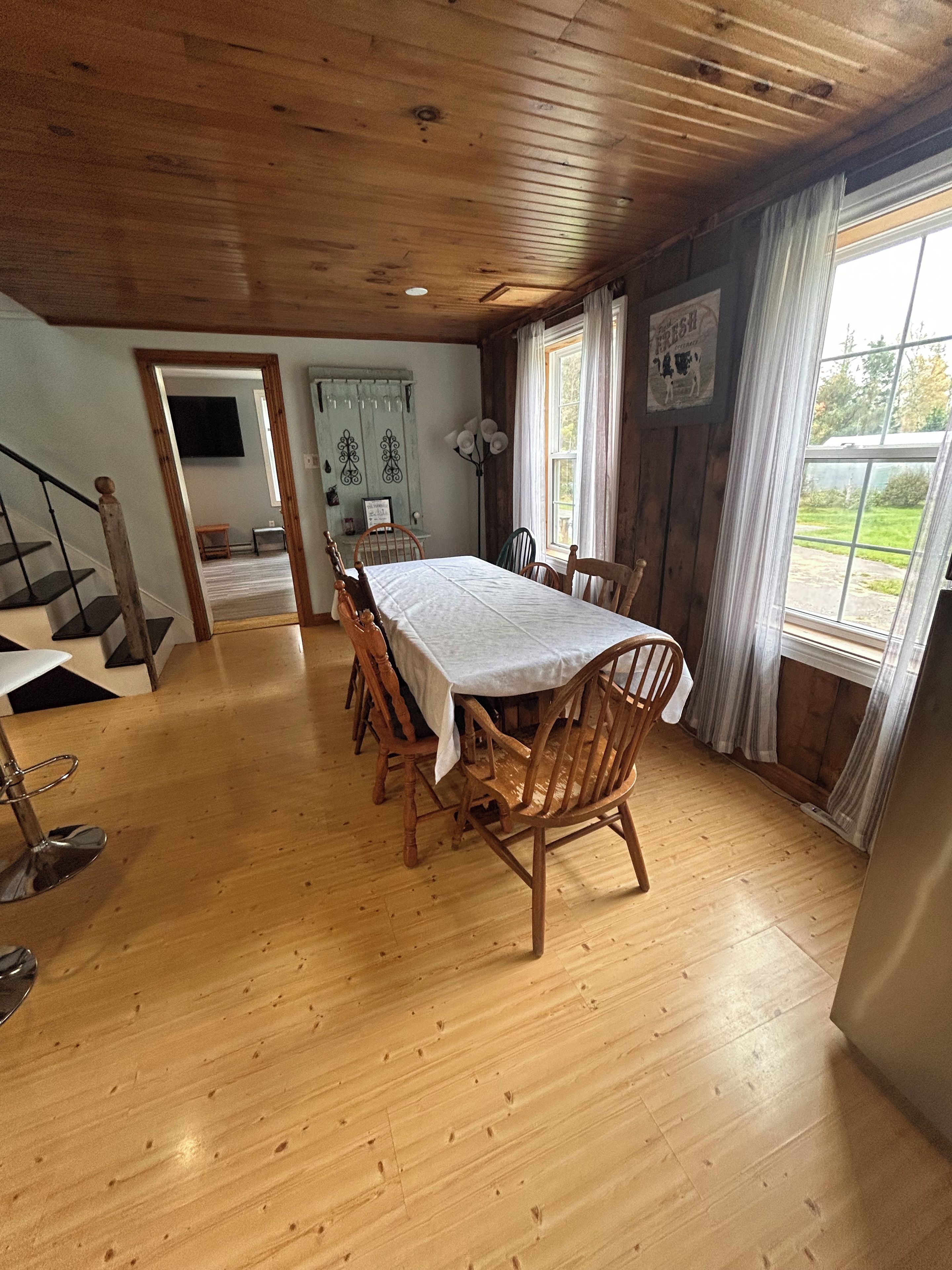 Un espace repas avec une table et des chaises en bois, un escalier et une vue sur l’extérieur.