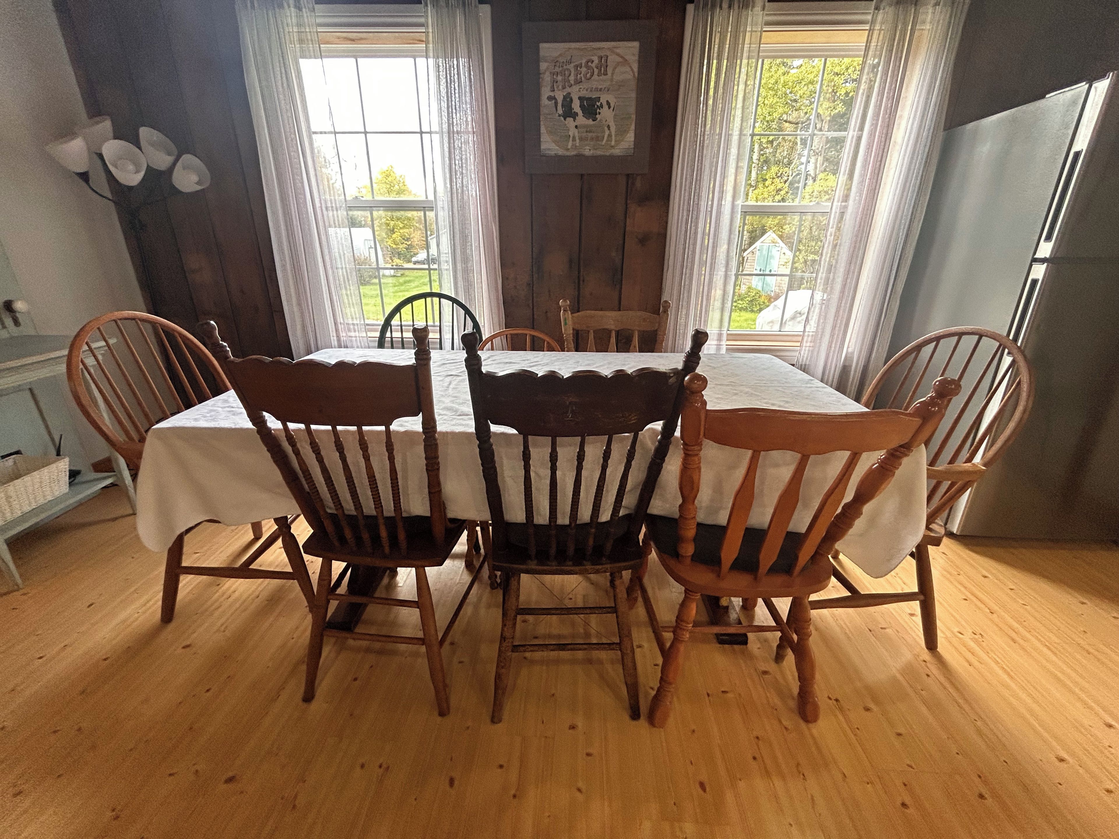 A dining area with a wooden table and chairs, a window with curtains, and a refrigerator.