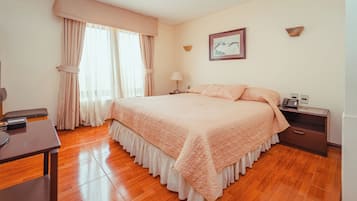 Un dormitorio con una cama grande, un escritorio, una silla, una mesita de noche, una lámpara y un cuadro en la pared.