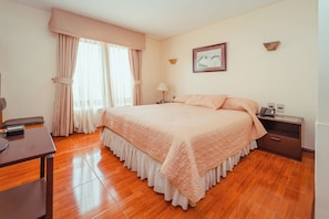 A bedroom with a large bed, a desk, a chair, a nightstand, a lamp, and a painting on the wall. - Hotel Francisco de Aguirre Costa (La serena)