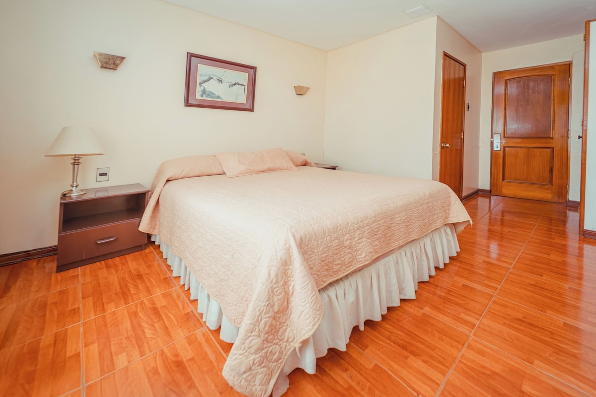 A bedroom with a bed, nightstand, lamp, and a door.