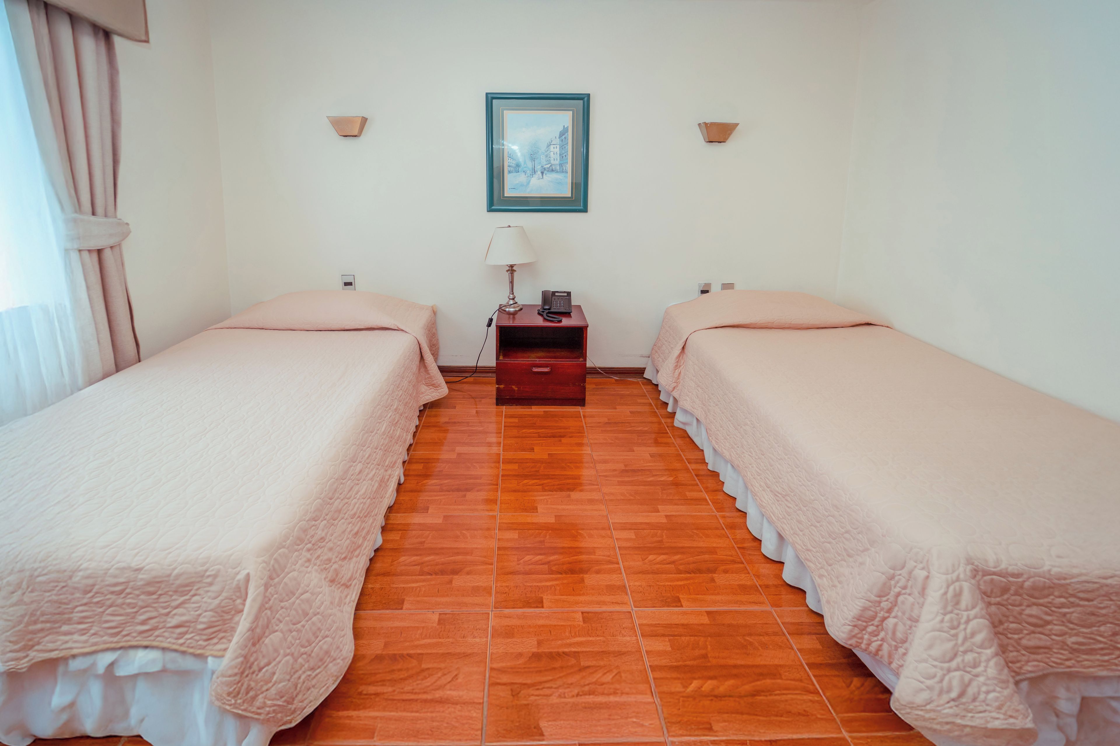 Une chambre d’hôtel avec deux lits, une table de chevet, une lampe et un tableau encadré au mur.