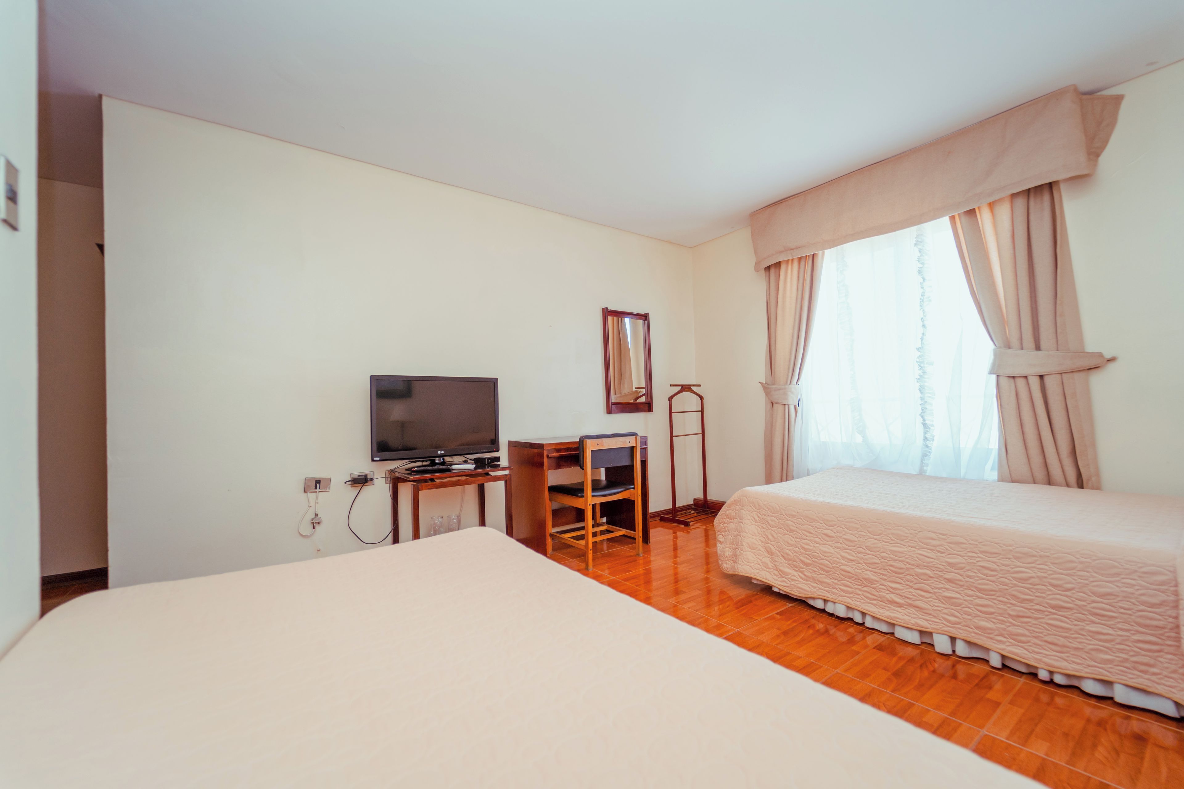A hotel room with a bed, a TV, a desk, and a window with curtains.